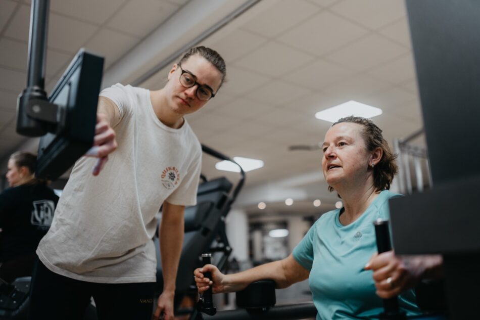Fitnesstrainer erklärt einer Frau am Gerät die Funktion